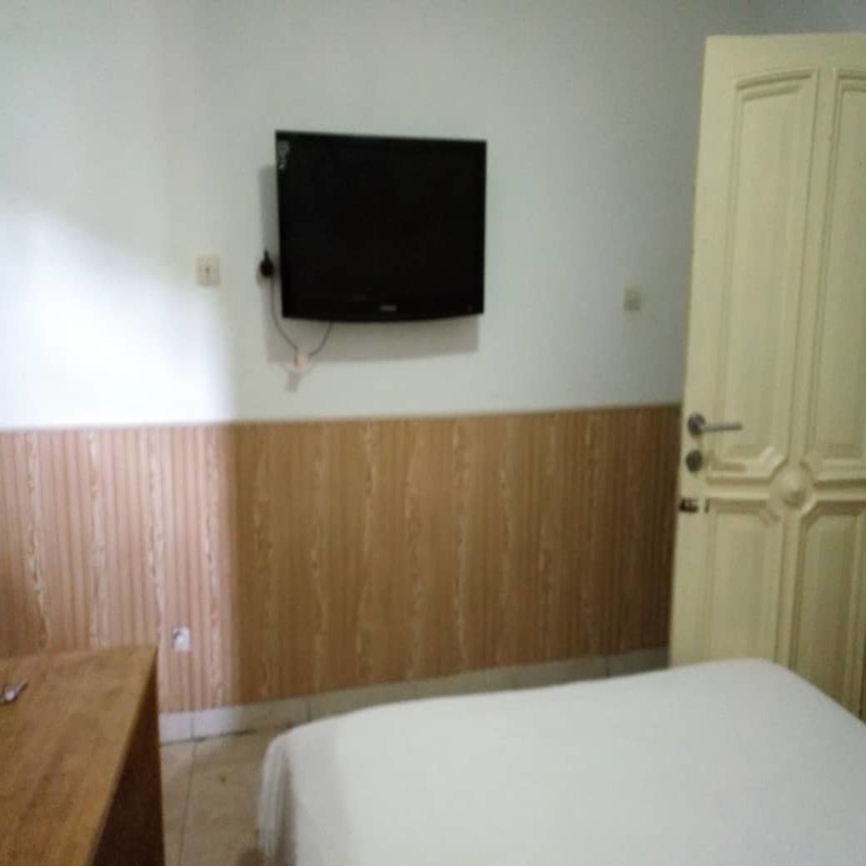 A room with a bed, a wooden desk, a television mounted on the wall, and a door.