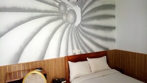 Een hotelkamer met een bed, een houten nachtkastje, een stoel en een muurschildering.