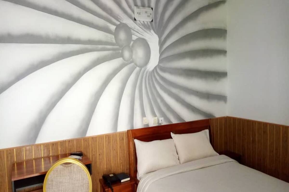 Ein Hotelzimmer mit einem Bett, einem Nachttisch aus Holz, einem Sessel und einem Wandbild.