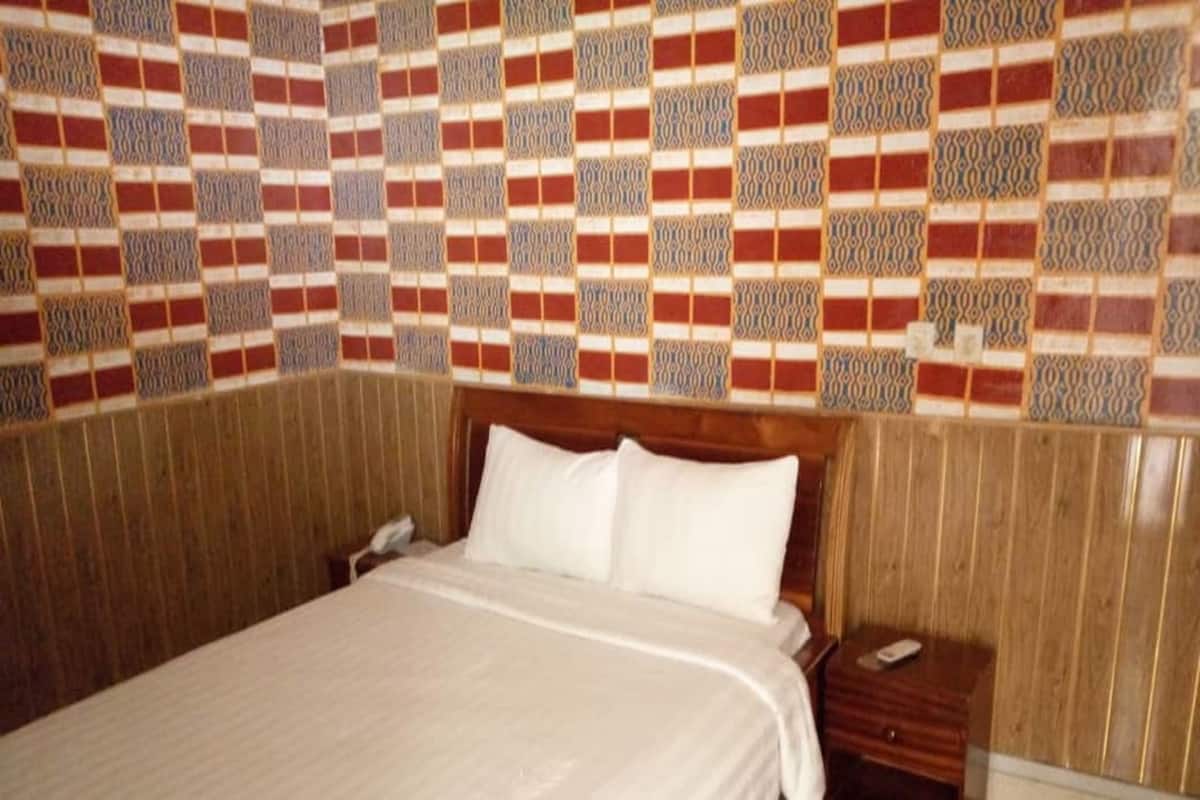 Ein Hotelzimmer mit einem großen Bett, einem Holzkopfteil, einem Nachttisch mit Telefon und einer Wand mit Muster.