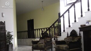 A spacious living area with two ornate armchairs, a staircase, and a potted plant. - Margalla Lodge (Islamabad)