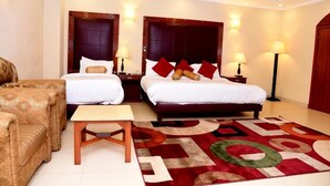 A hotel room with two beds, a sofa, a small table, and a decorative rug. - Hotel Pak Heritage (Lahore)