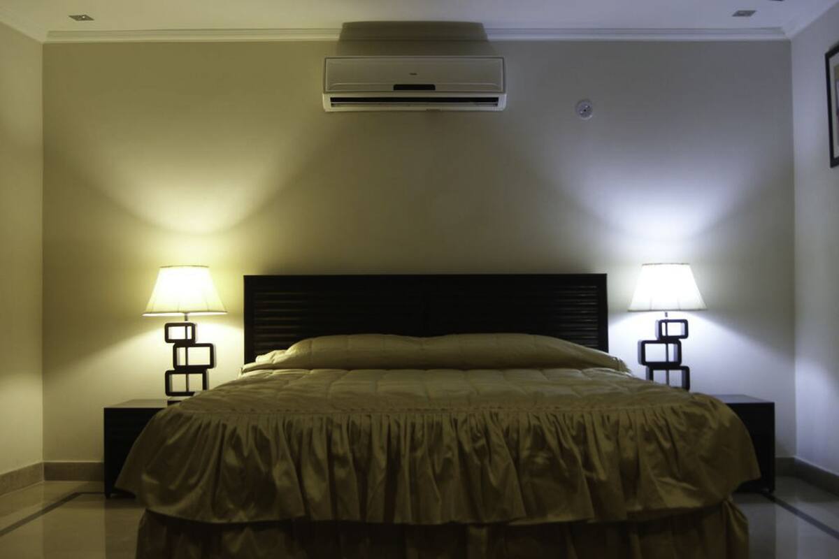 Une chambre d’hôtel comprenant un lit, deux lampes de chevet, un appareil de climatisation et une table de chevet.