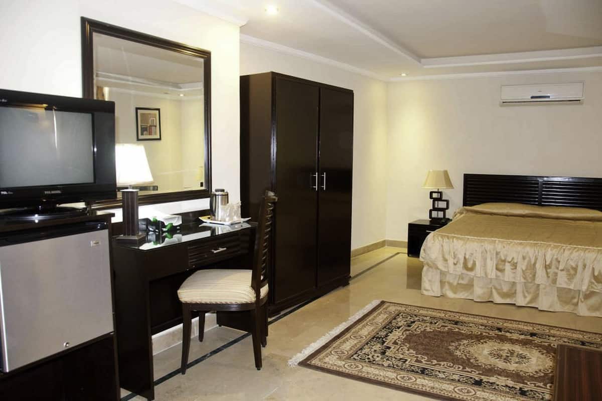 Une chambre d’hôtel comprenant un lit, un bureau avec une chaise, une télévision, une armoire et un tapis.