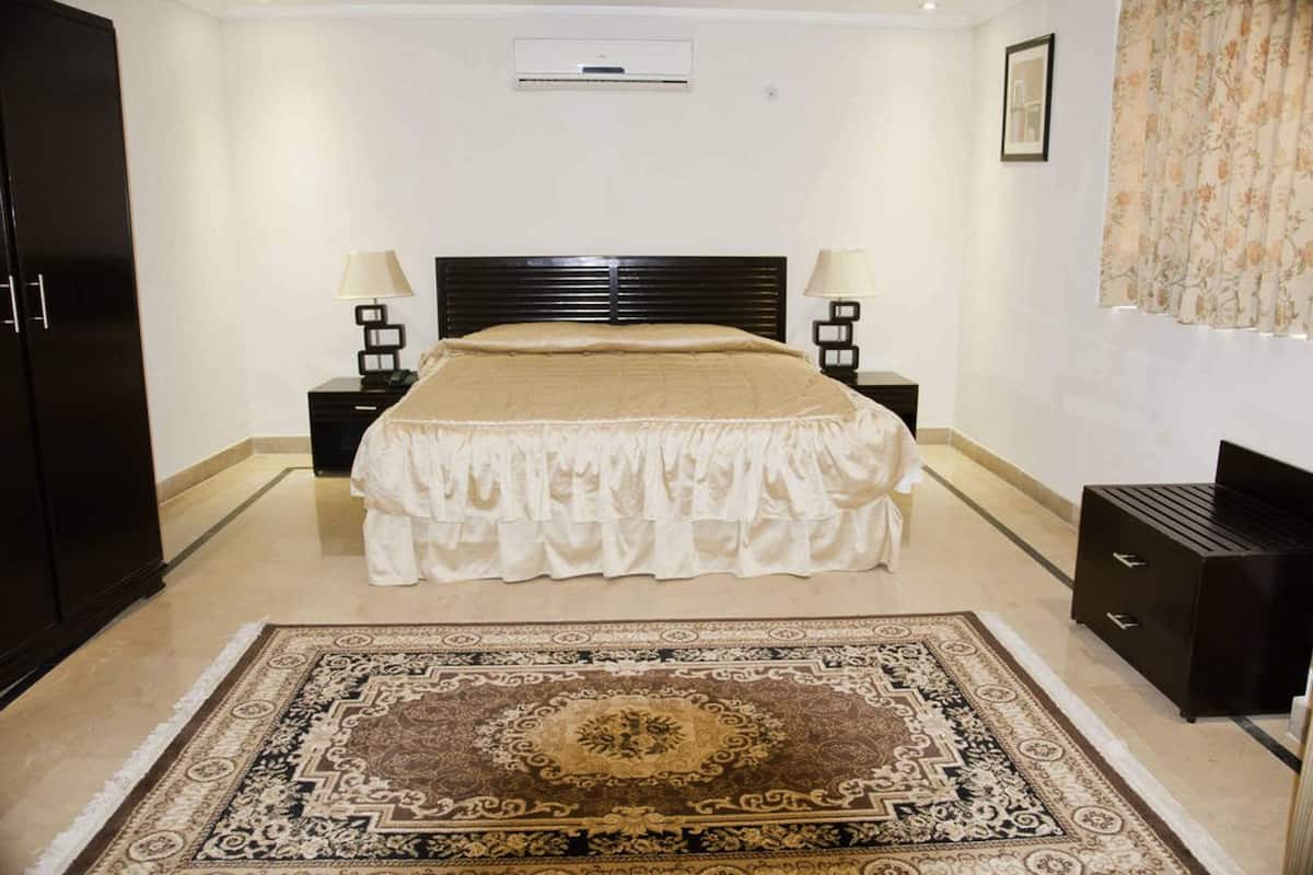 Une chambre à coucher avec un grand lit, deux tables de chevet avec des lampes, une armoire sombre et un tapis à motifs.
