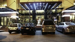 A hotel entrance with a covered walkway, multiple cars parked in front, and a person in white attire standing near the entrance. - Hotel Pak Heritage (Lahore)