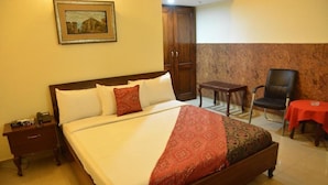 Een hotelkamer met een groot bed, een houten nachtkastje, een stoel, een kleine tafel en een kledingkast.