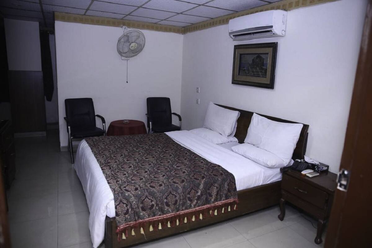 Ein Schlafzimmer mit einem Bett, zwei Stühlen, einem Nachttisch, einer Klimaanlage und einem Wandventilator.