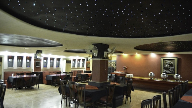 Een restaurant met een sterrenhemel, meerdere eettafels met stoelen en een bar.
