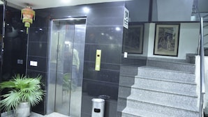 Een lift met glazen deur, een prullenbak en een trap.
