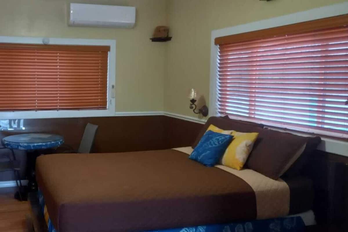 A room with a bed, a small round table, and two windows with blinds.