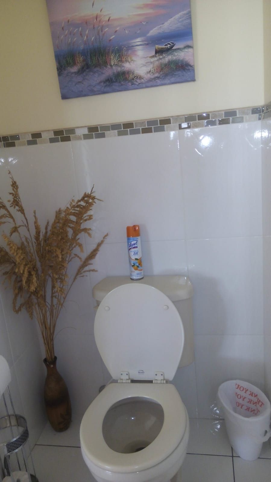 Une salle de bain avec des toilettes, un vase contenant des plantes séchées et un tableau accroché au mur.