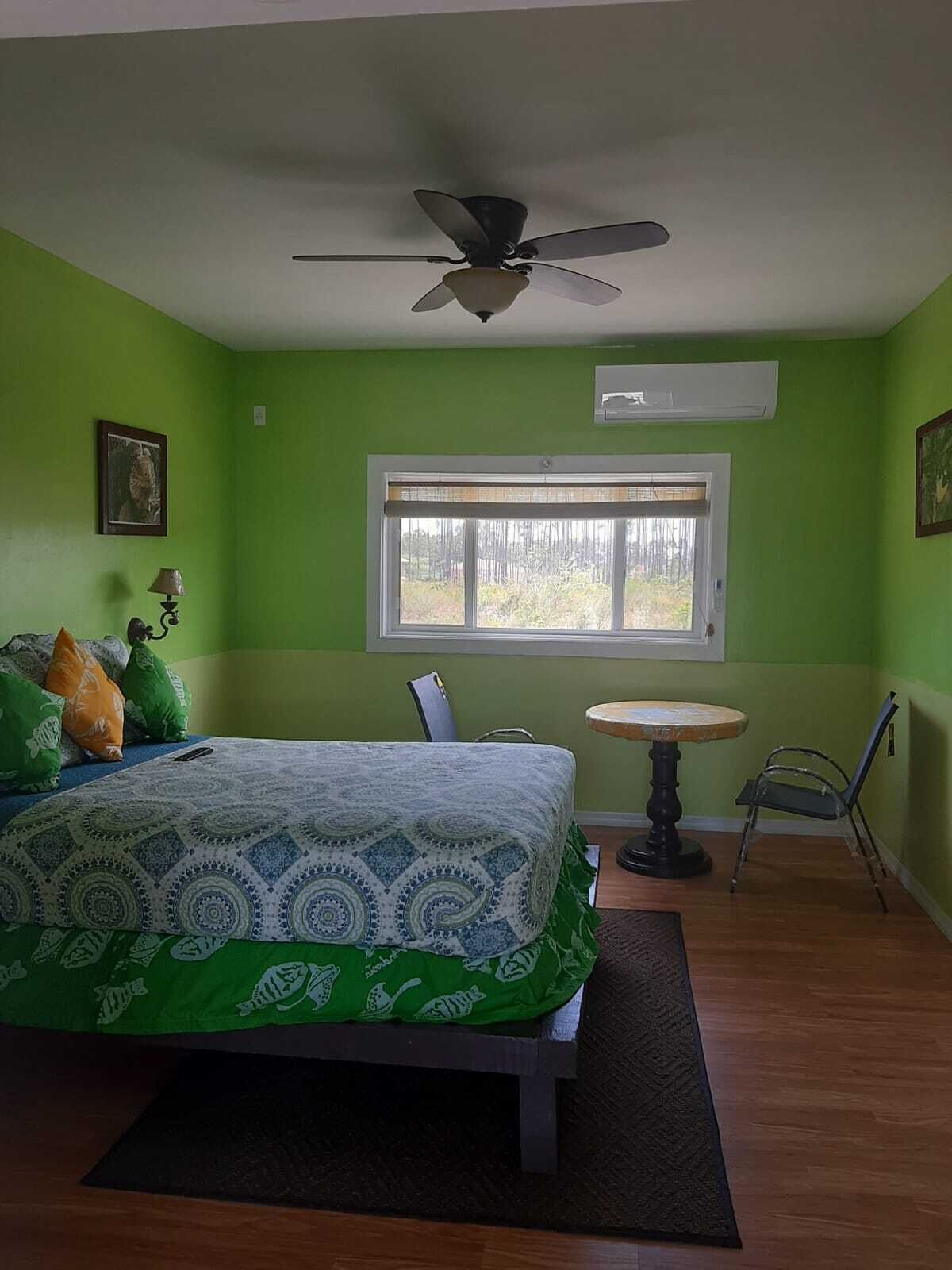 A bedroom with a bed, a ceiling fan, a window, a table, and a chair.