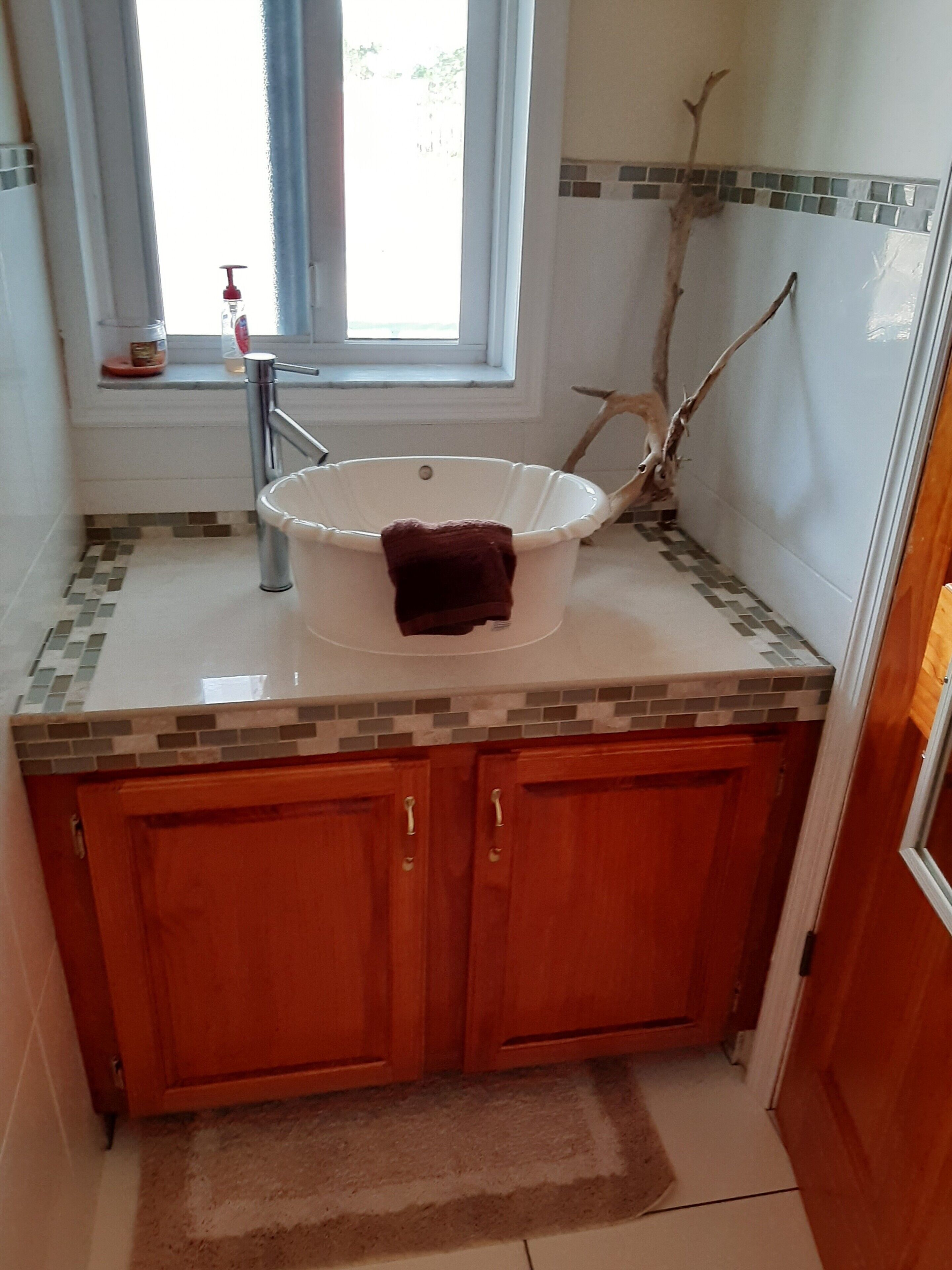 Ein Badezimmer mit einer weißen Badewanne, Holzschränken, einer gefliesten Rückwand und einem Fenster mit Blick.