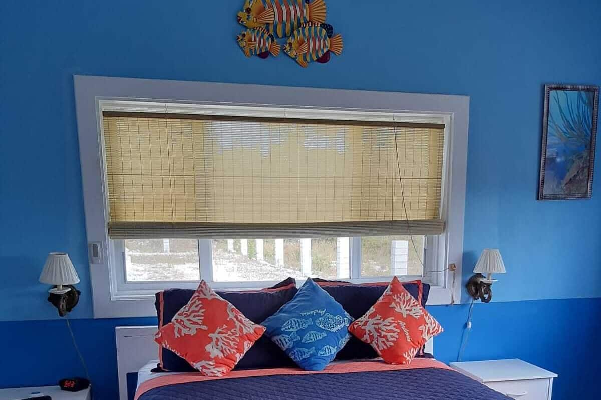 A bedroom with a large bed, a window with blinds, two bedside tables with lamps, and a wall decoration.