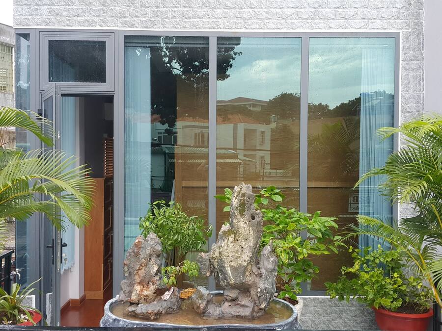 Um edifício moderno com grandes janelas de vidro, fachada de pedra e um pequeno jardim de rochas com plantas em vasos.