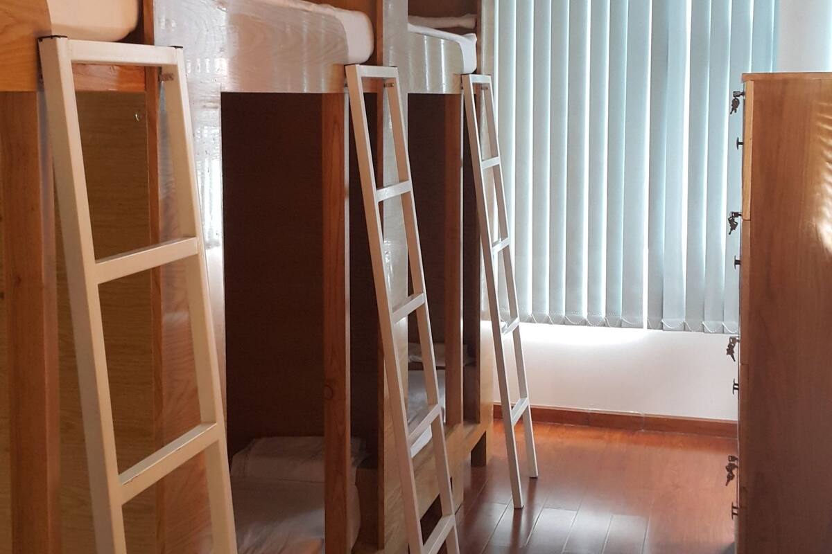A room with bunk beds, wooden ladders, a window with blinds, and a wooden cabinet.