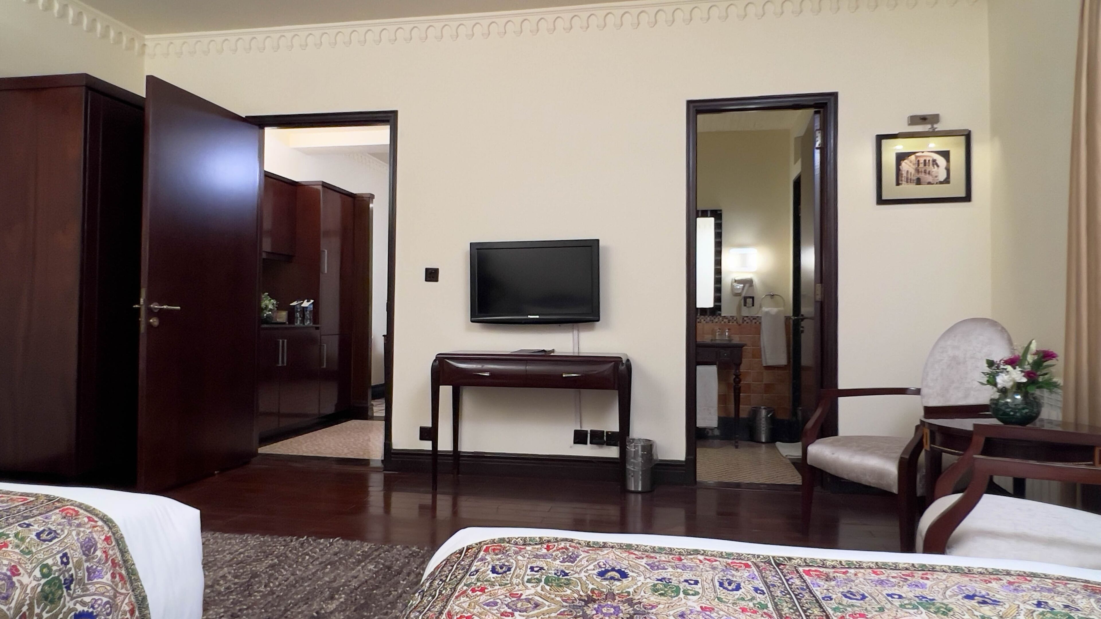 A hotel room with a bed, a desk, a television, a chair, a mirror, and a bathroom visible through an open door.