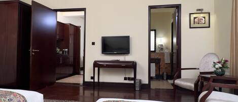 Habitación de hotel con cama, escritorio, televisor, sillón, espejo y baño visible a través de una puerta abierta.
