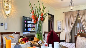 Ein Frühstücksbrett mit Eiern, Toast, Obst und Kaffee, eine Blumenvase sowie ein Fernseher, der verschiedene Sender zeigt.