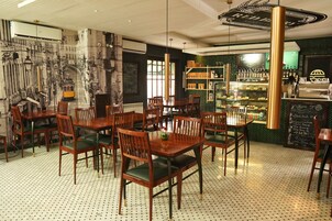 A restaurant interior with wooden tables and chairs, a bar area with shelves of bottles, and a chalkboard menu.