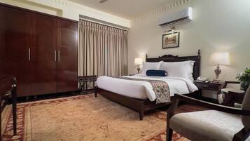 A hotel room with a large bed, a wardrobe, a desk with a lamp, and an air conditioning unit.