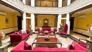 Eine geräumige Lobby mit roten Sofas, einem zentralen Couchtisch mit Blumenarrangement und einem dekorativen Spiegel über der Sitzecke.