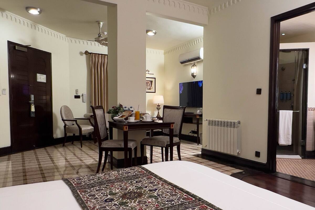 Ett hotellrum med en säng, ett matbord med stolar, en tv och ett badrum som syns genom en öppen dörr.