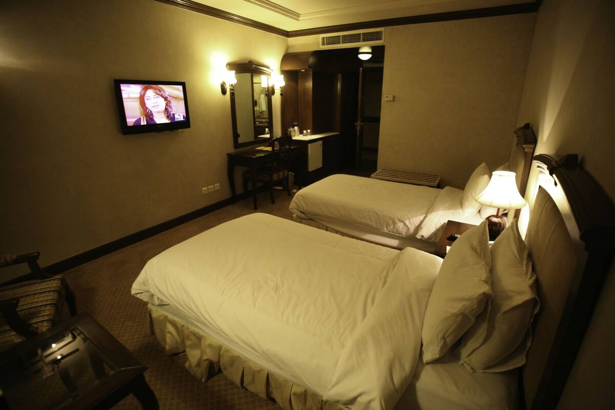 A hotel room with two beds, a desk, a television, and a mirror.