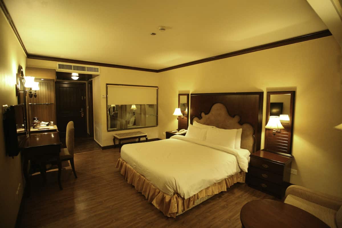 A hotel room with a large bed, a desk, a chair, and a mirror.
