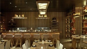 Un restaurante con una larga mesa de madera dispuesta para comer, rodeada de sillas blancas.