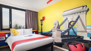 A hotel room with a bed, a view of a cityscape, a mural of a bridge, and a statue of a lion. - Ibis Styles Budapest Citywest (Budapest)