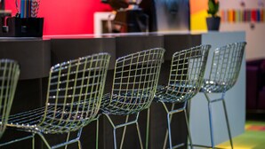 A row of wireframe chairs in a modern setting with a red wall and a bar area in the background. - Ibis Styles Budapest Citywest (Budapest)