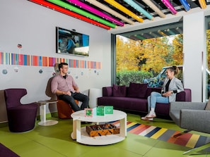 A modern interior with a large window, a sofa, a coffee table, and a wall-mounted TV. - Ibis Styles Budapest Citywest (Budapest)