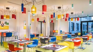 A modern dining area with multiple tables and chairs, overhead colorful pendant lights, and large windows. - Ibis Styles Budapest Citywest (Budapest)