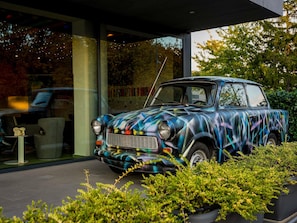 A vintage car parked in front of a modern building with glass doors and a visible outdoor seating area. - Ibis Styles Budapest Citywest (Budapest)