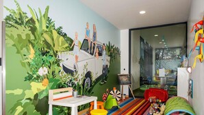 A child's playroom with a mural, colorful striped carpet, and a green tunnel. - Ibis Styles Budapest Citywest (Budapest)