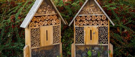 Dos casas de pájaros de madera con varios compartimentos para anidar, rodeadas de follaje denso.