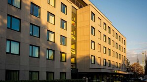 A multi-story hotel with a modern design, featuring a central staircase, large windows, and a parking area with a bicycle. - Ibis Styles Budapest Citywest (Budapest)