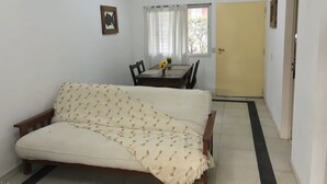 A room with a sofa, a dining table with chairs, a window with curtains, and a door.