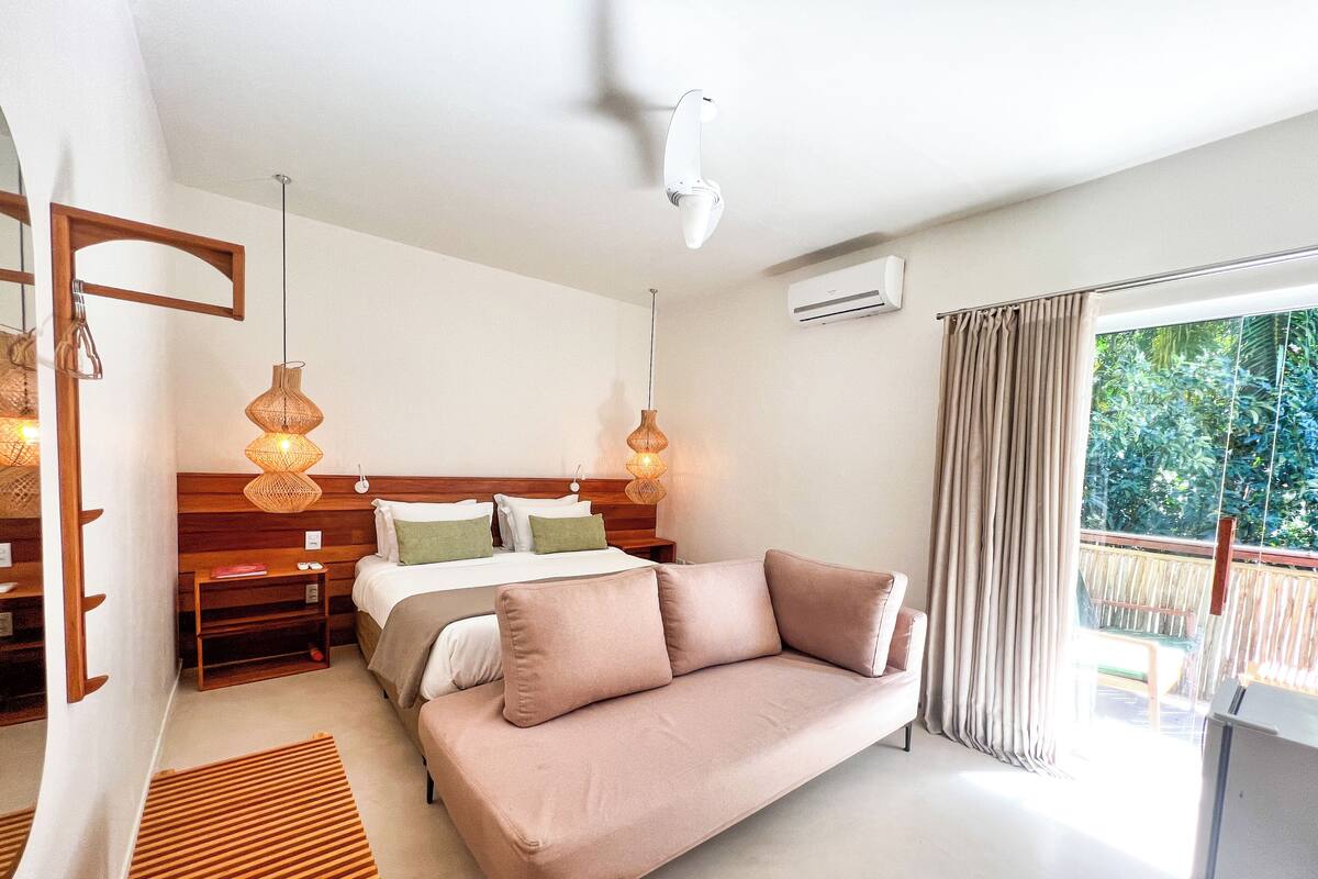 Un dormitorio con cama, sofá, cabecera de madera y ventana con cortinas.