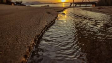 Escena de playa con un cuerpo de agua tranquilo, un puente de madera y un atardecer al fondo.