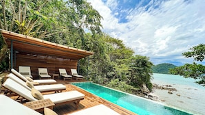 Terraza de madera con sillones de descanso y una piscina con vista a la playa.