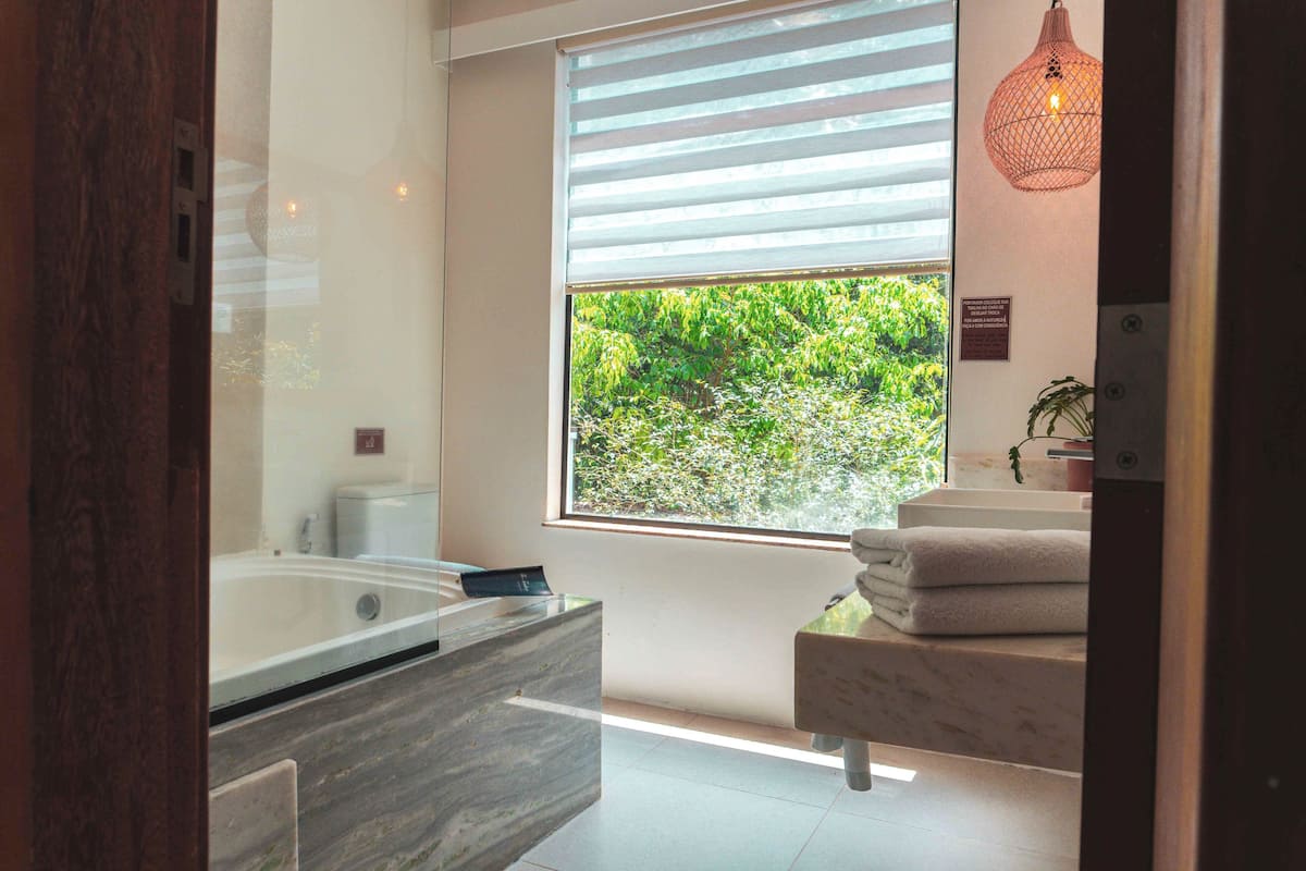 Un baño moderno con una ventana grande, una bañera, un tocador de mármol y una lámpara colgante.