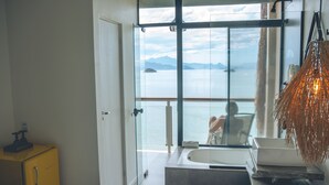 Un baño moderno con una bañera grande, cabina de ducha con vidrio y vista al mar.