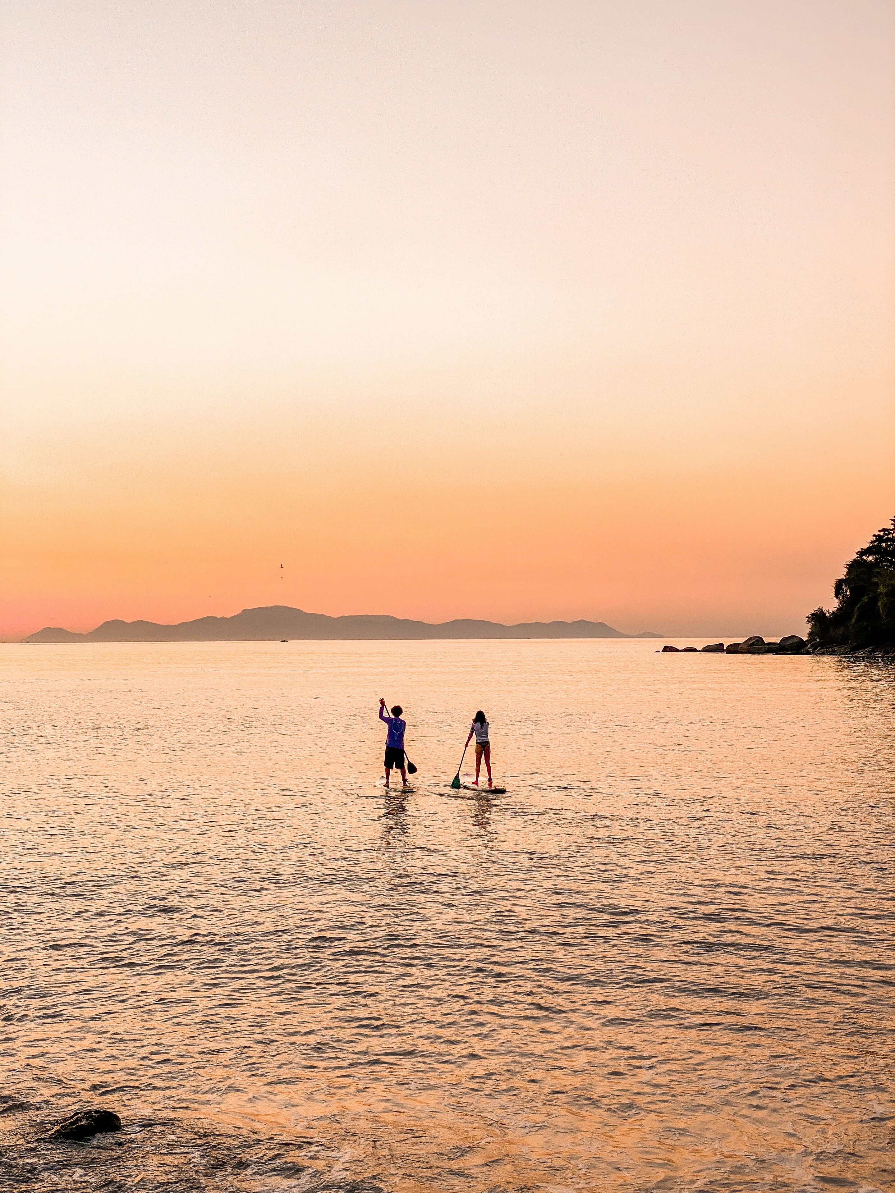 Dos personas practican paddleboard en aguas tranquilas durante la puesta de sol.
