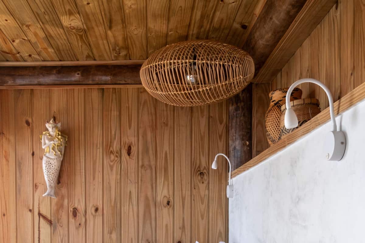 Una habitación tipo cabaña de madera con una cama, una lámpara de fibra tejida y una luz empotrada en la pared.