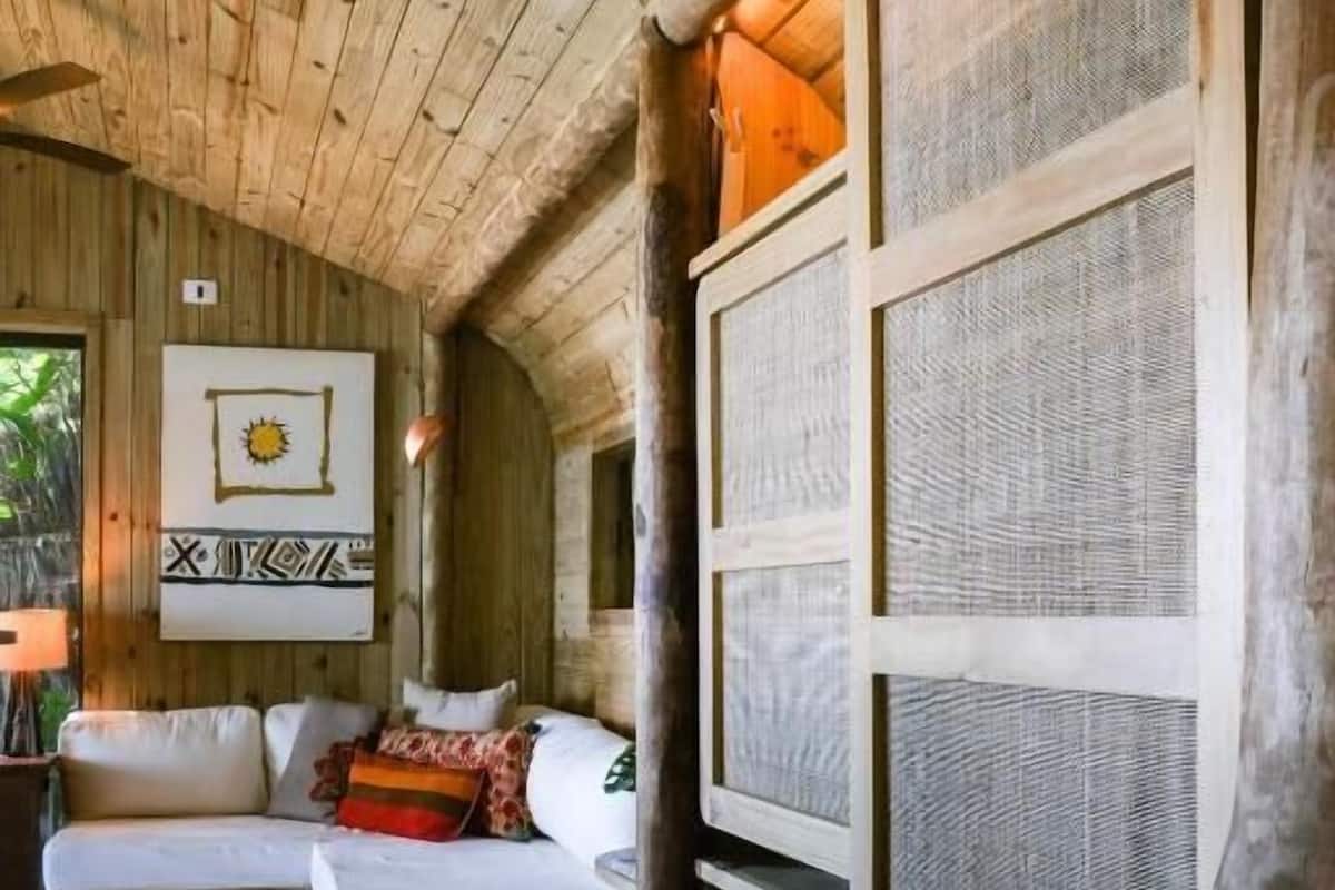 Un interior de madera con un sofá, un separador tejido y un cuadro en la pared.