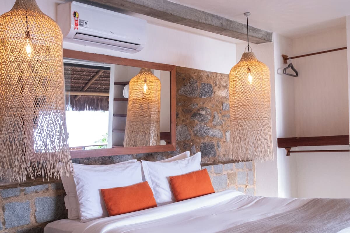 Un dormitorio con una cama grande, dos mesitas de noche, una pared de detalles en piedra y una lámpara colgante.