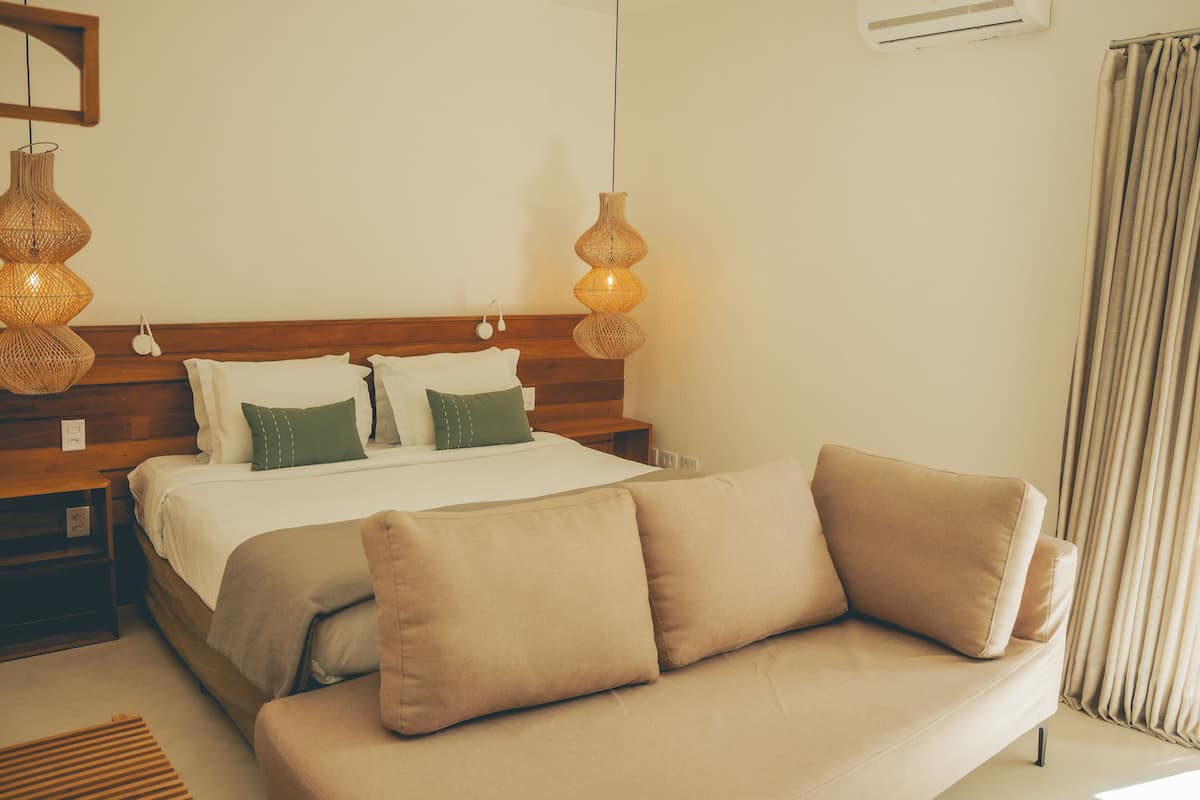 Un dormitorio ordenado con una cama, dos mesitas de noche, un sofá y lámparas colgantes.